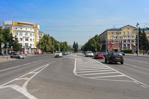 A bustling urban street scene with cars, trees, and historic buildings under a clear sky.