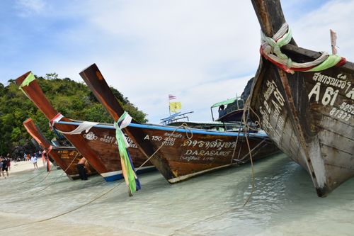 Free Long-tail boats anchored on a picturesque tropical beach with clear water and green hills. Stock Photo
