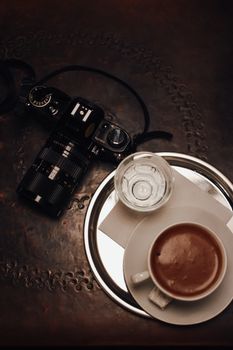 Overhead view of a vintage camera and coffee cup on a dark rustic table. Perfect for lifestyle or travel themes.