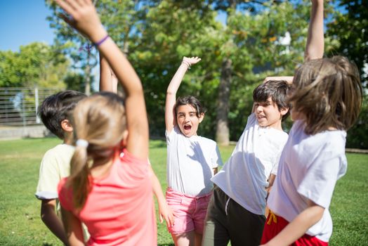 Group of children playing with raised arms in a sunny park, enjoying summer fun.