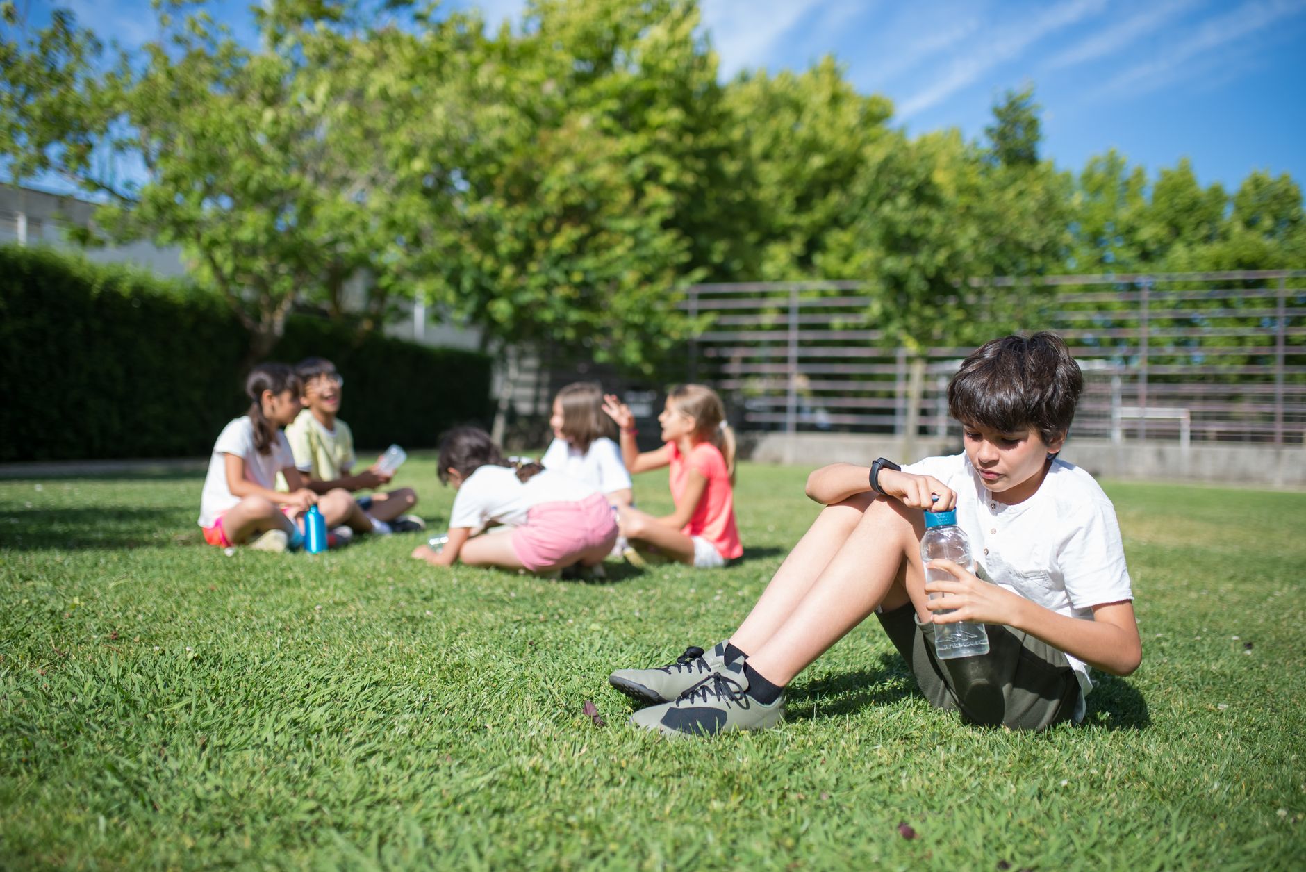 Group of children relaxing and playing on grass in a sunny park, enjoying the outdoors.