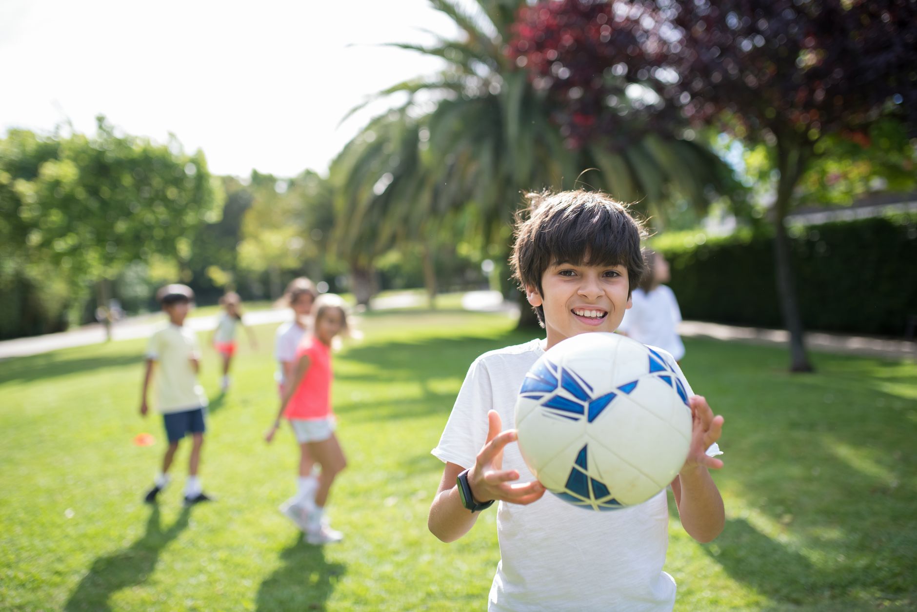 Group of children playing football outdoors in a sunny park with joy and excitement.