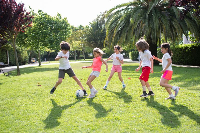 Group of kids enjoying a game of soccer in a lush green park on a sunny day