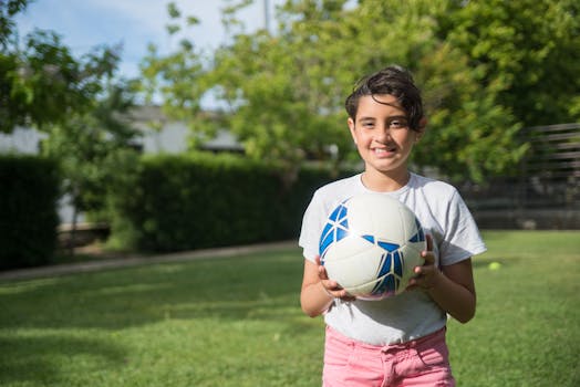 Smiling girl holding a soccer ball in a sunny park in Portugal, ideal for sports-themed content.