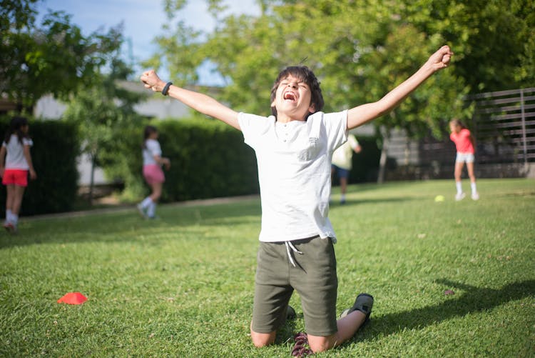 Victorious Boy Kneeling On Grass 