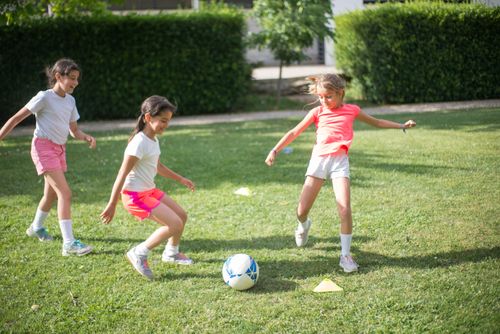 Free Three young girls having fun playing soccer outdoors on a sunny day. Stock Photo