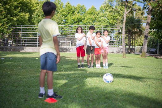 A group of kids enjoy a soccer game outdoors in a sunny park setting.