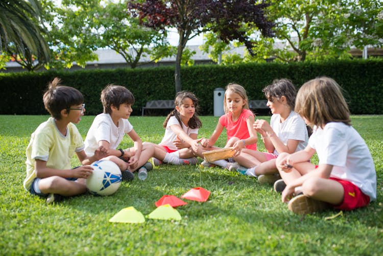 Kids Playing While Sitting On The Green Grass 