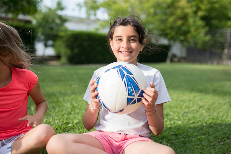 Girl In White Shirt Sitting On Grass Holding A Soccer Ball