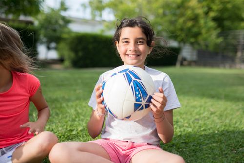 Free Happy young girl smiling while holding a soccer ball in a sunny outdoor park. Stock Photo