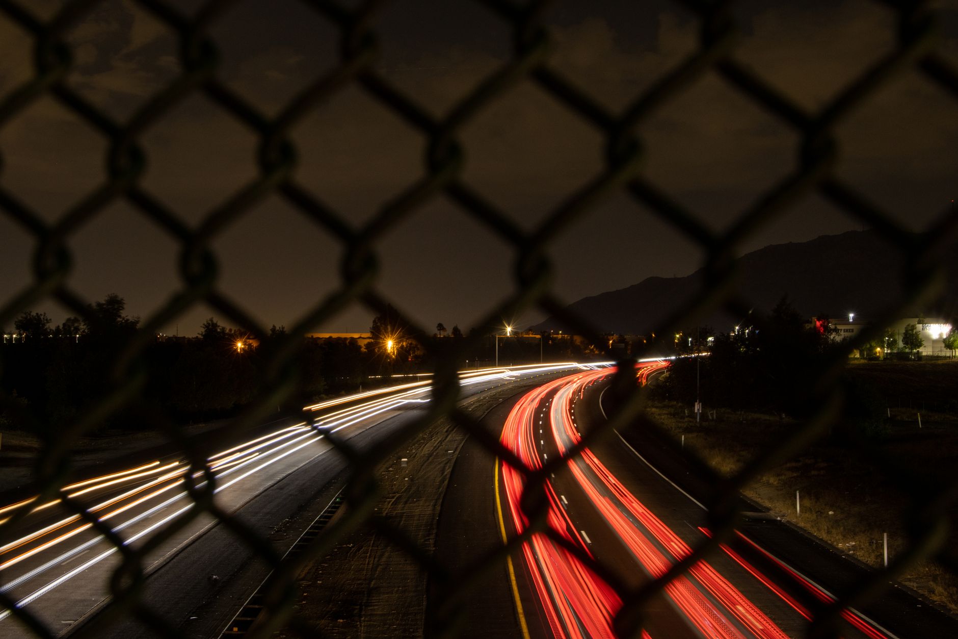 Night long exposure capturing car light trails through a chain link fence in Moreno Valley, CA.