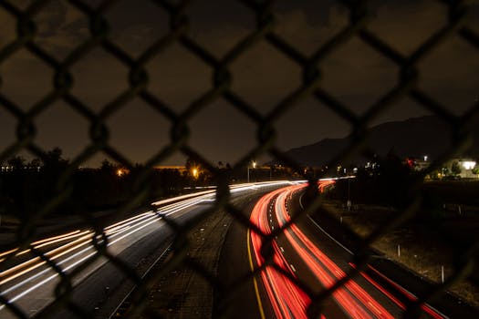 Night long exposure capturing car light trails through a chain link fence in Moreno Valley, CA.