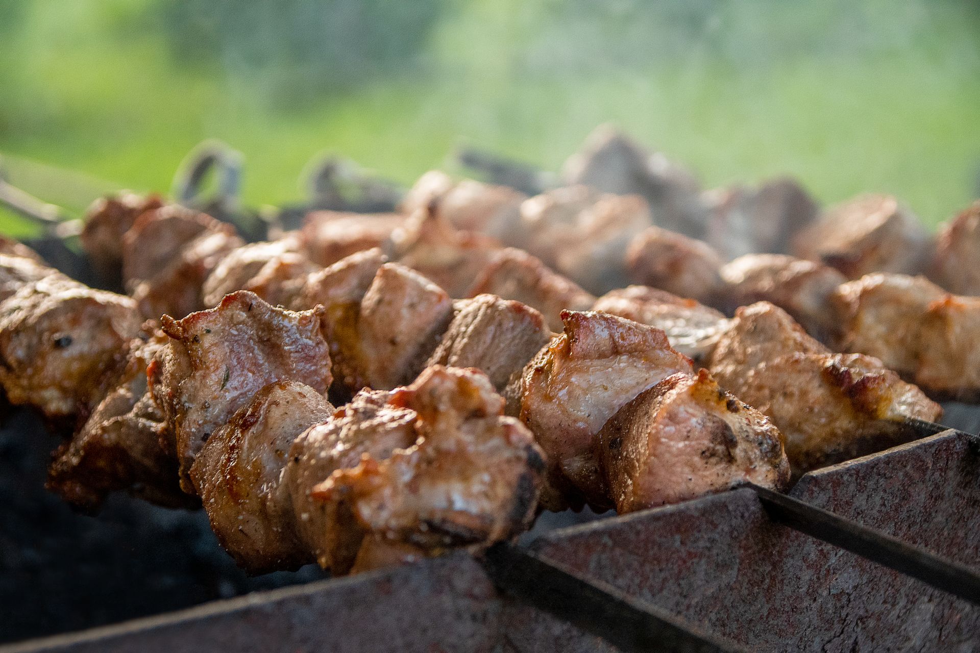 Juicy skewers of meat sizzling on a hot charcoal grill with smoke rising.