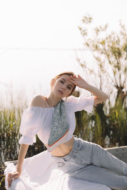 A stylish woman poses outdoors in a white off-shoulder top and denim jeans, exuding a casual and chic fashion style.