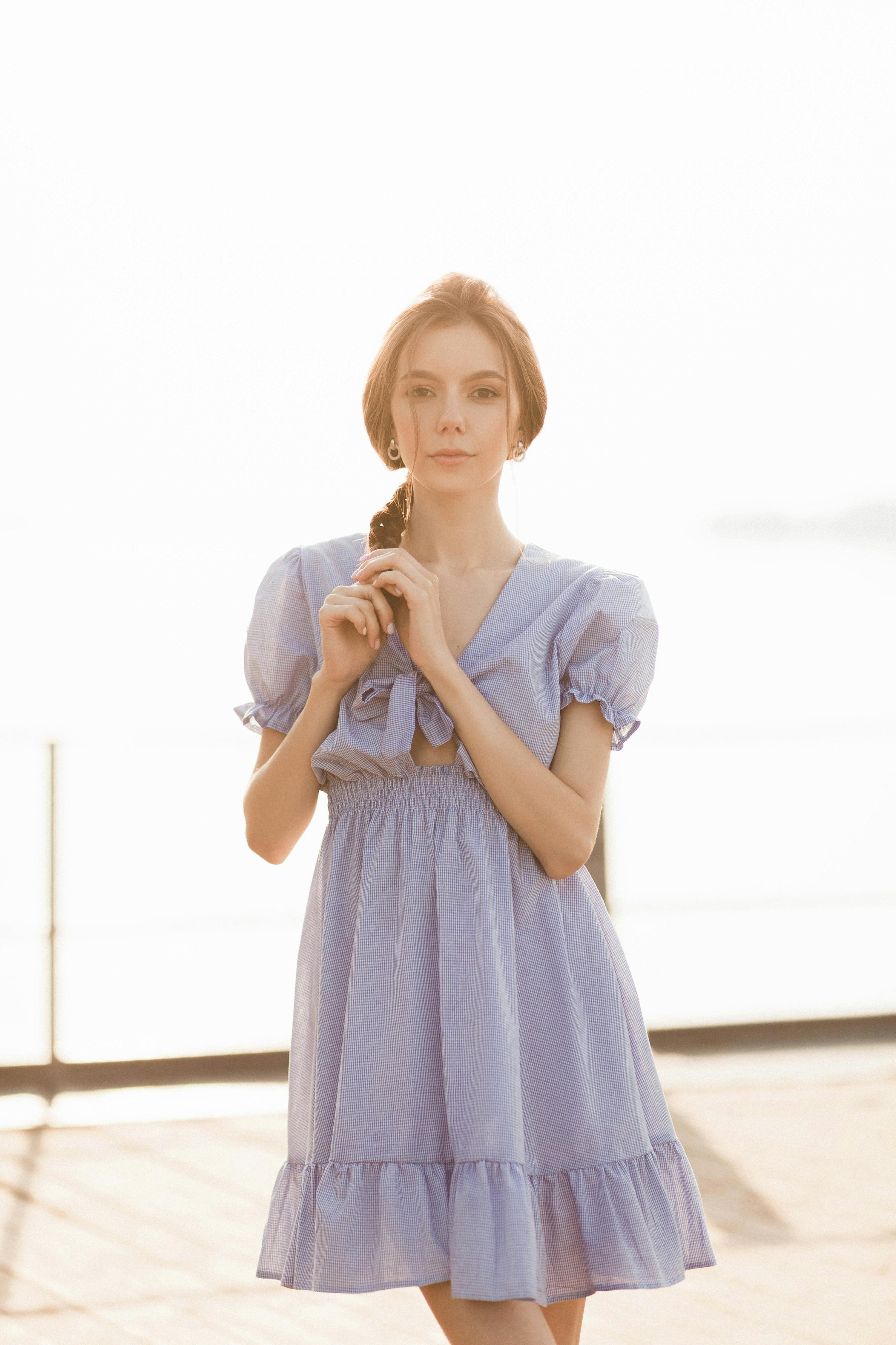 A stylish woman in a light blue dress poses outdoors with a serene expression, capturing elegance and fashion.