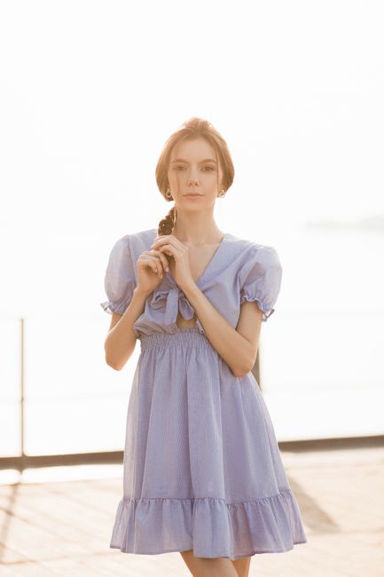 A stylish woman in a light blue dress poses outdoors with a serene expression, capturing elegance and fashion.
