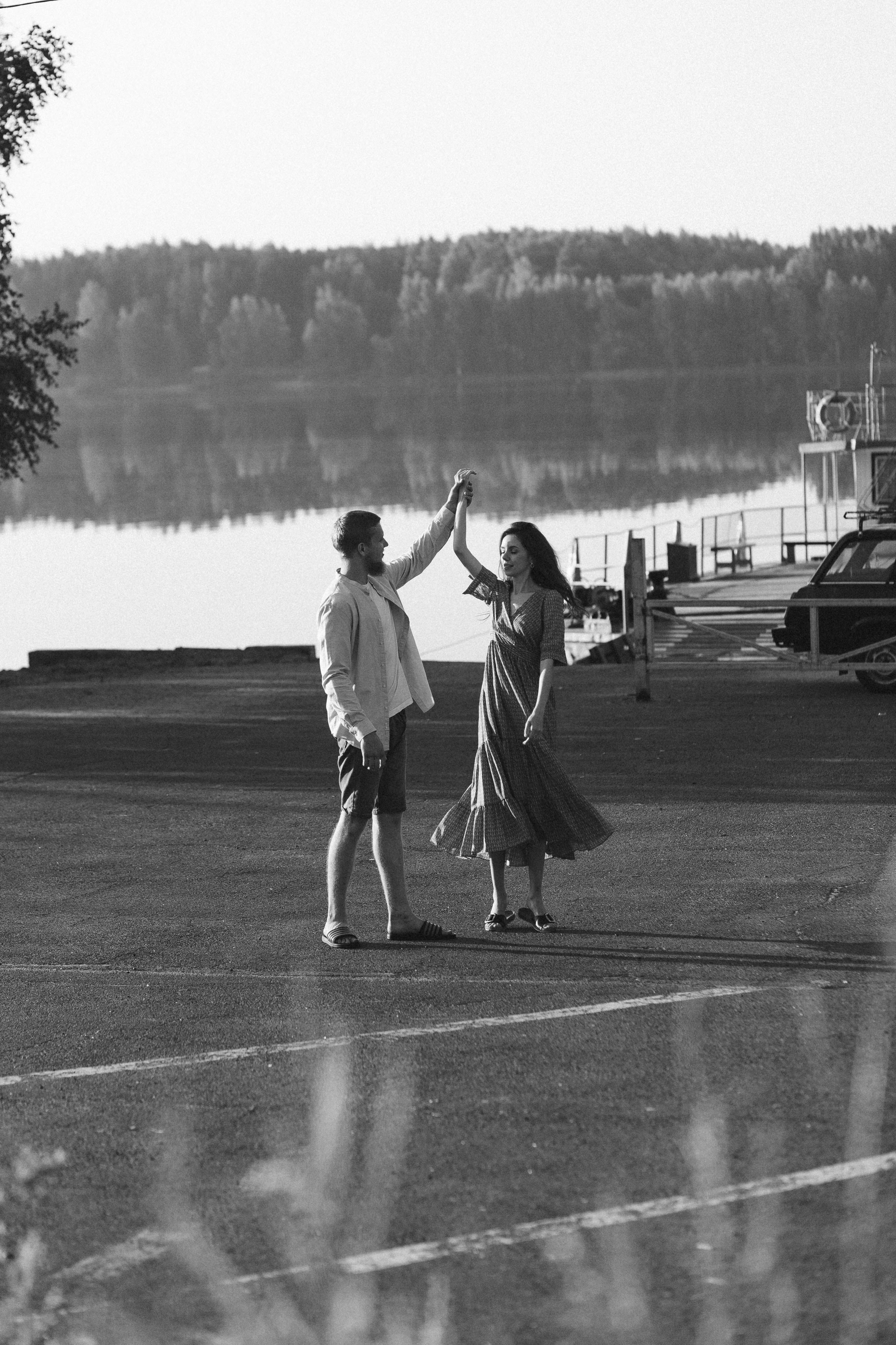A romantic couple dances happily by a calm lakeside, showing love and joy.