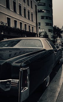 Rear view of a vintage classic car parked on a rainy city street, with a retro building backdrop.