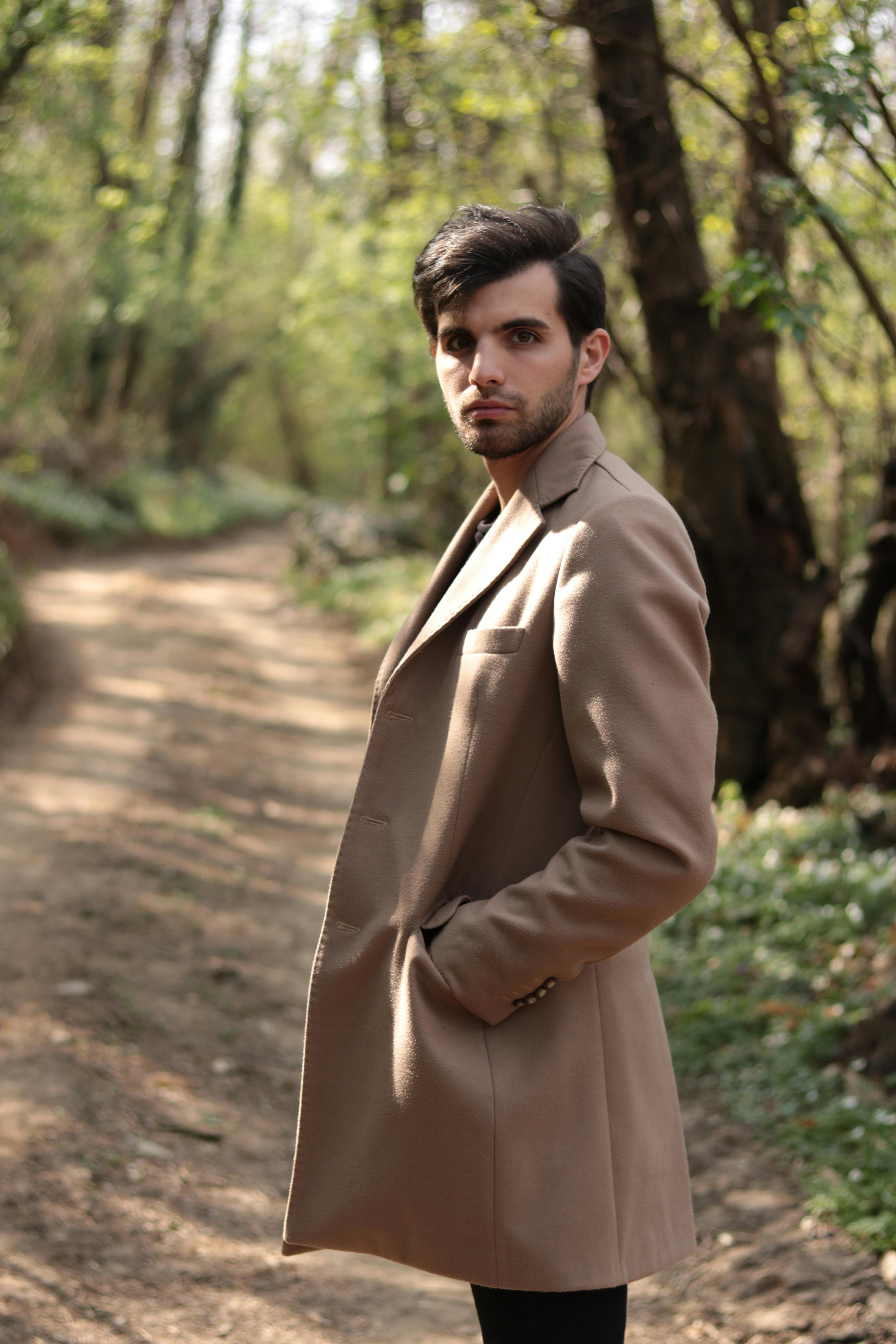 Bearded man in brown coat standing in woods