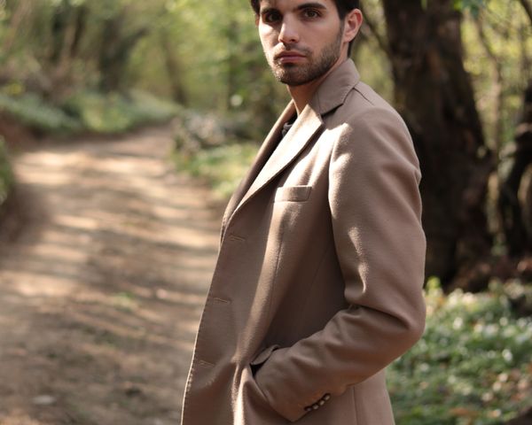 Bearded man in brown coat standing in woods