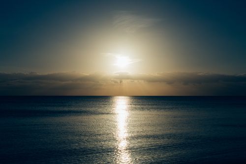 Free Serene view of a sunset over calm ocean waters, casting a warm glow. Stock Photo