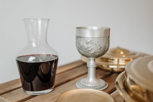 Free Close-up of a pewter goblet and red wine decanter on a wooden table, capturing elegance and tradition. Stock Photo