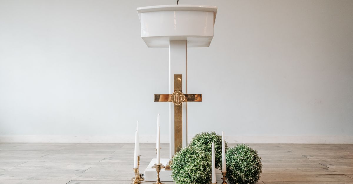 A minimalistic church altar setup featuring a white podium, golden cross, and decorative candles.