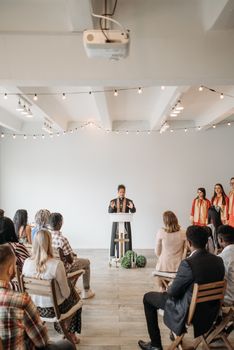 A diverse audience attends a ceremony with a speaker at a podium in a well-lit indoor setting.