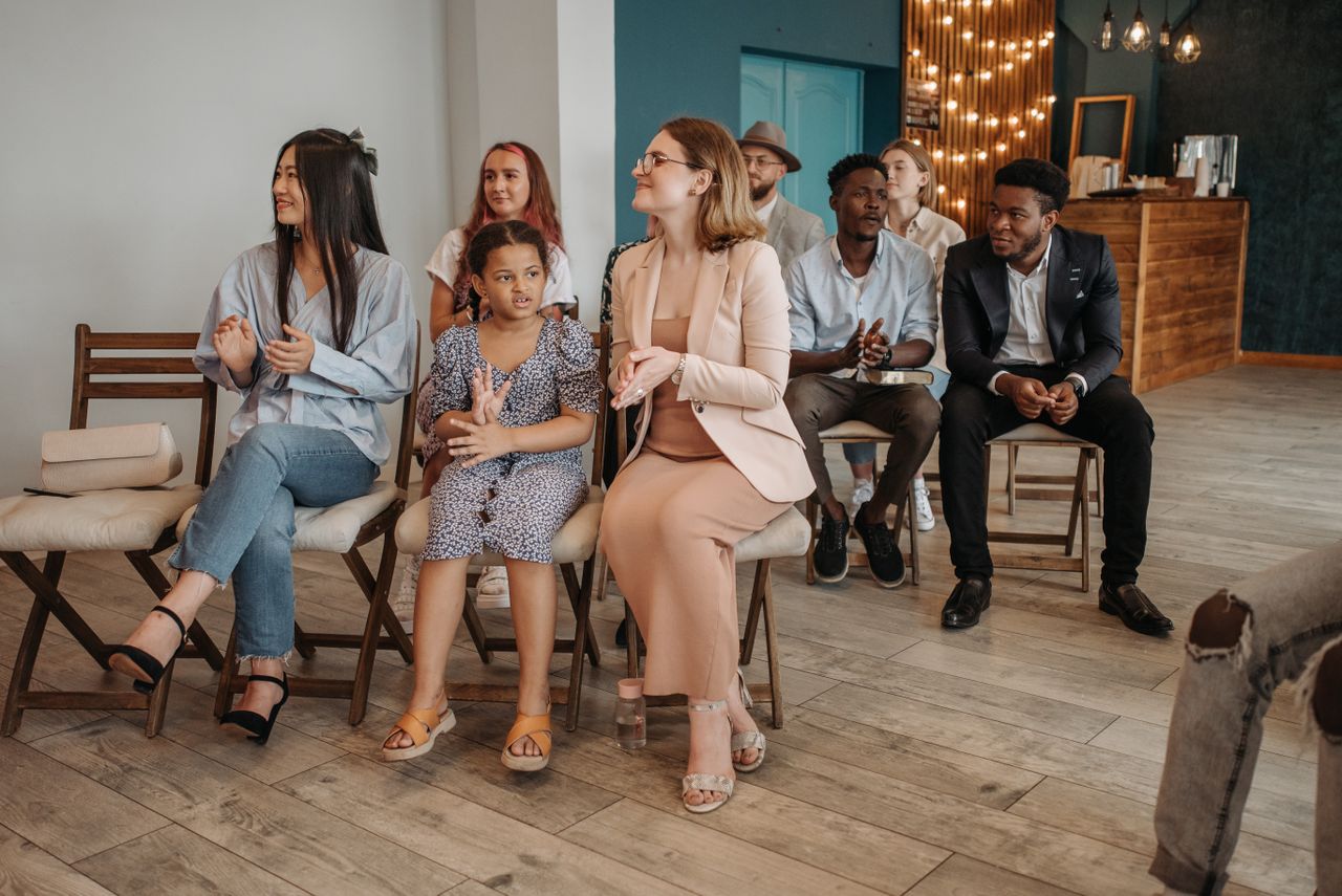 A diverse, well-dressed audience sitting and clapping in a modern indoor setting