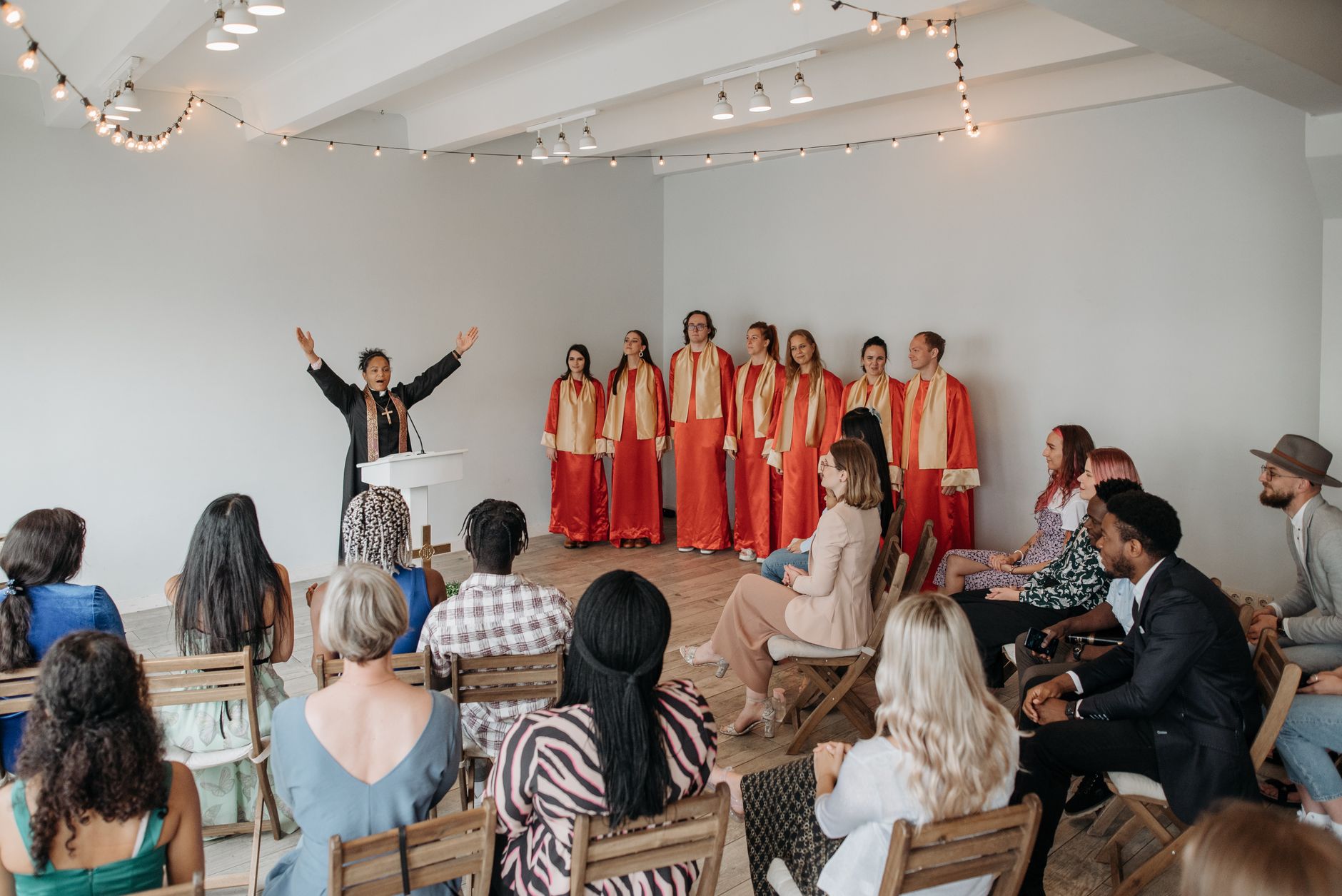 A vibrant choir performing for a congregation led by a female pastor in a church hall.