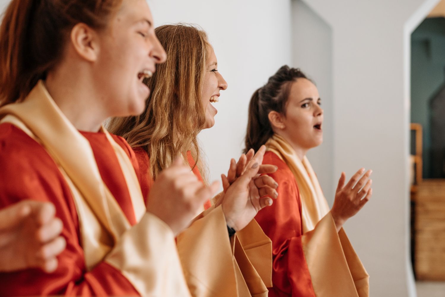 Three women in red choir mantles joyfully singing inside a church