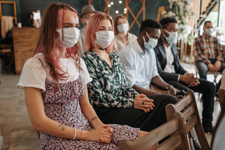 Women And Men In Face Masks Sitting On Chairs In A Row