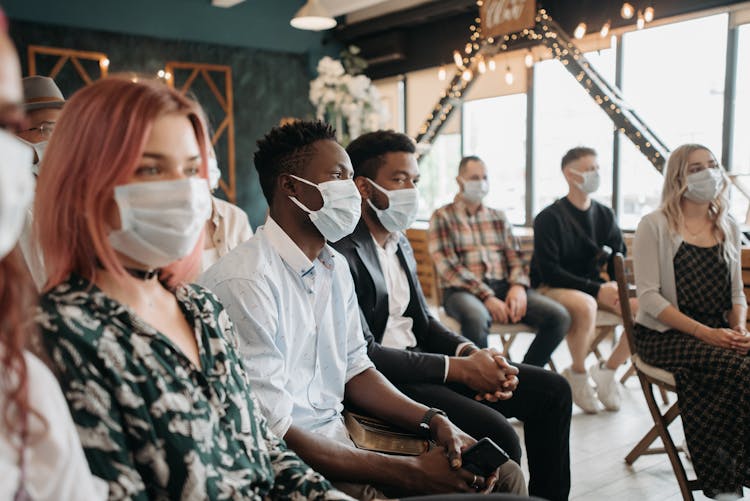 Group Of People Sitting In A Room Wearing Face Masks