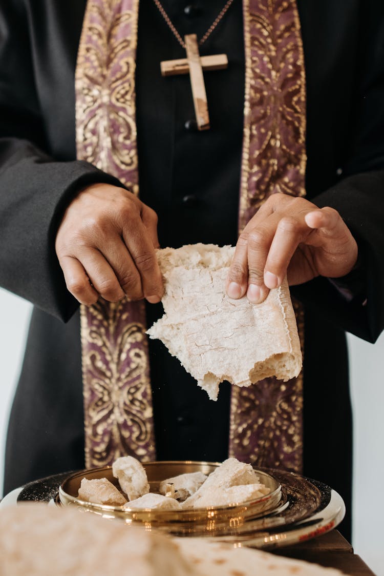 A Pastor In Black Long Sleeves Breaking Bread