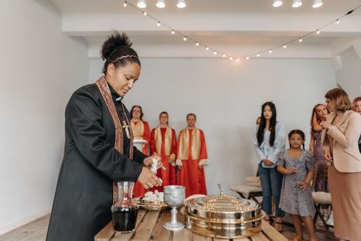 A diverse group of people attending a religious ceremony with a priest performing rituals indoors.