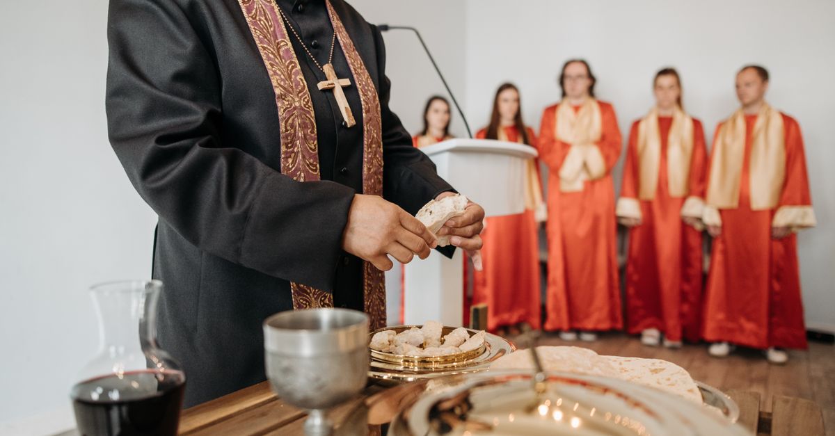A pastor conducts communion during a church service with a choir in the background.