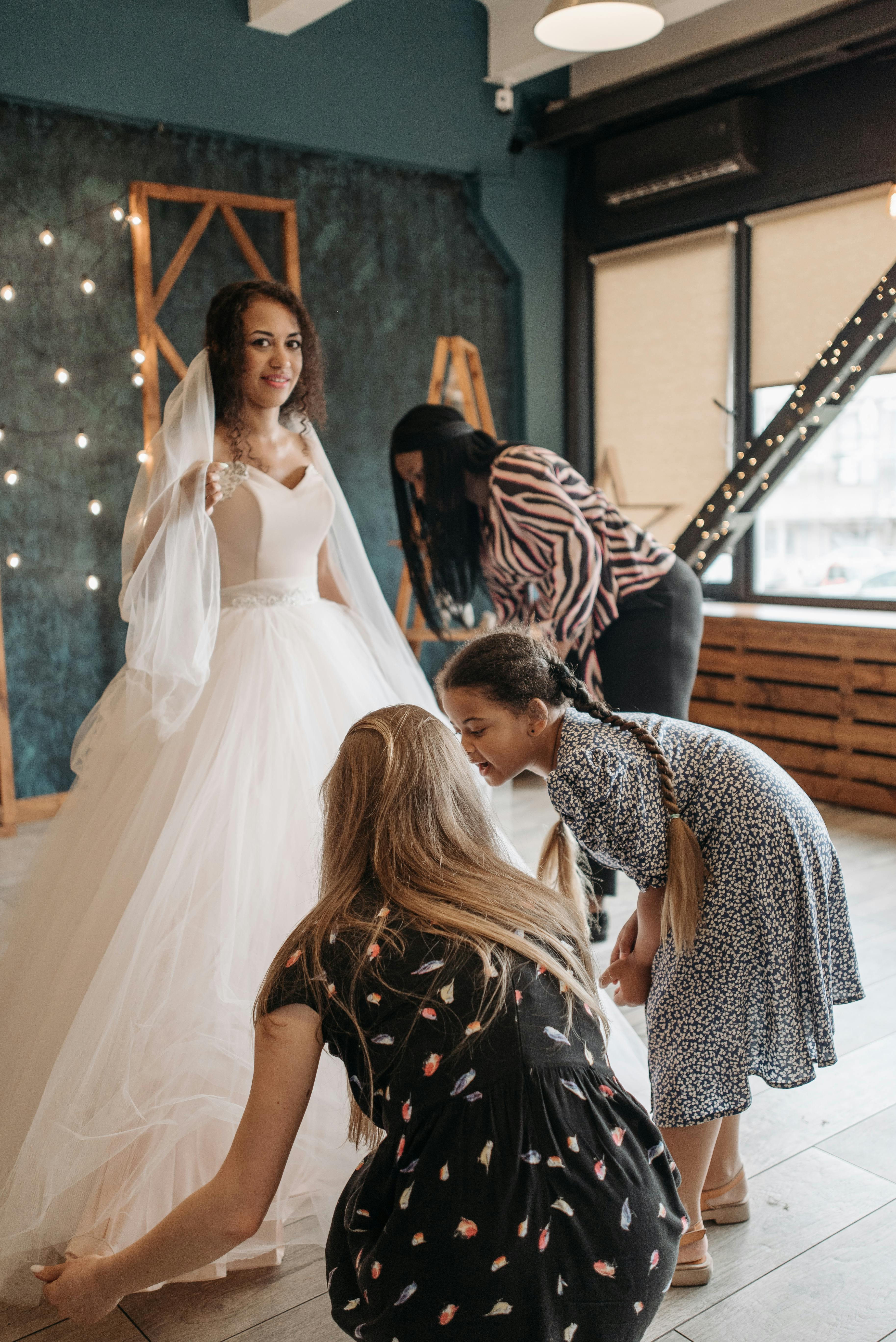Bride in gown with assistants preparing for her wedding day indoors.