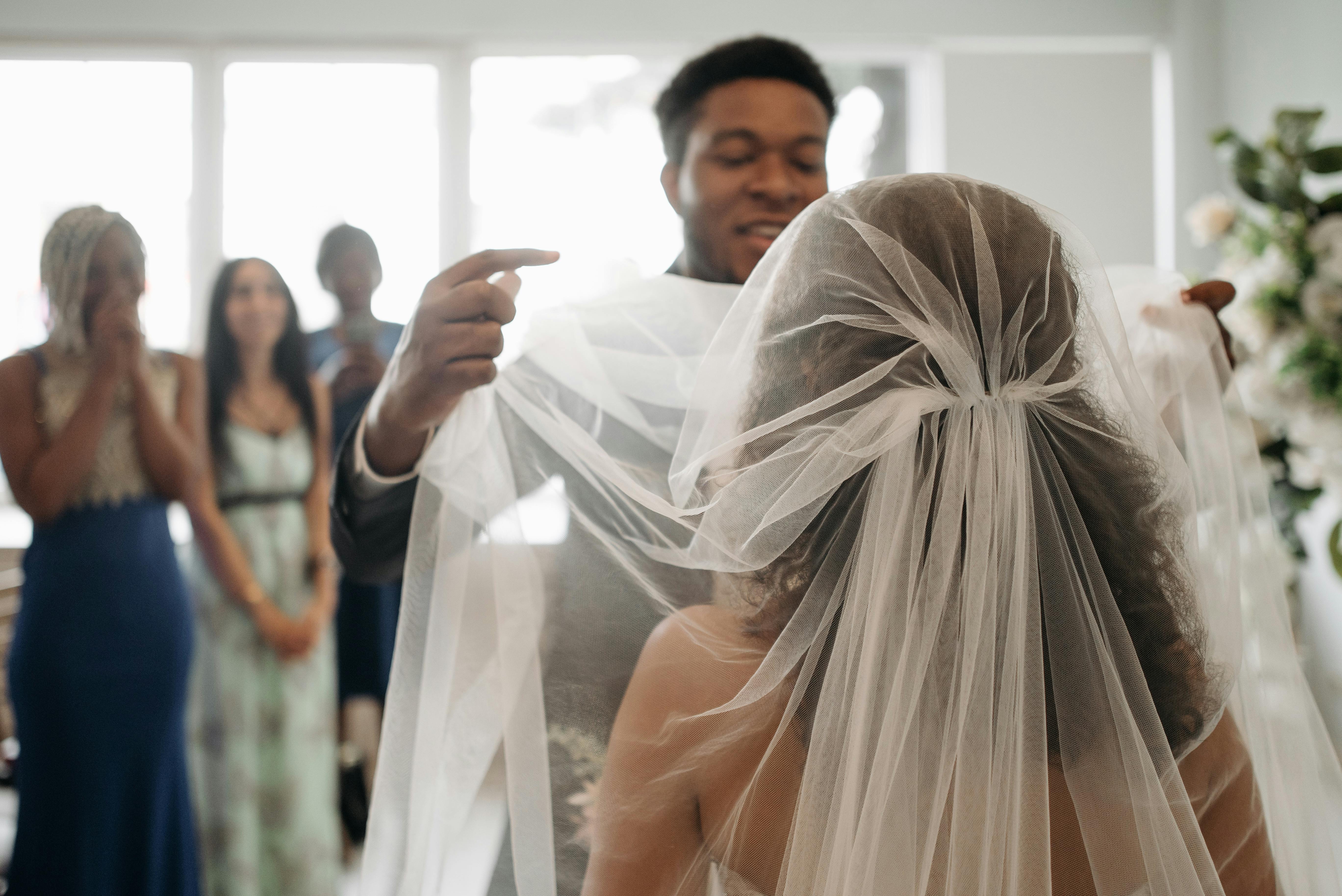 A groom lifting the bride's veil with guests watching at a wedding ceremony.