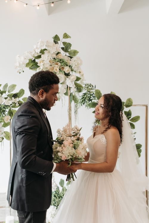 Free Bride and groom share a moment during an elegant indoor wedding ceremony with floral decorations. Stock Photo