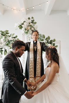 A romantic indoor wedding ceremony with a pastor blessing a couple holding hands.