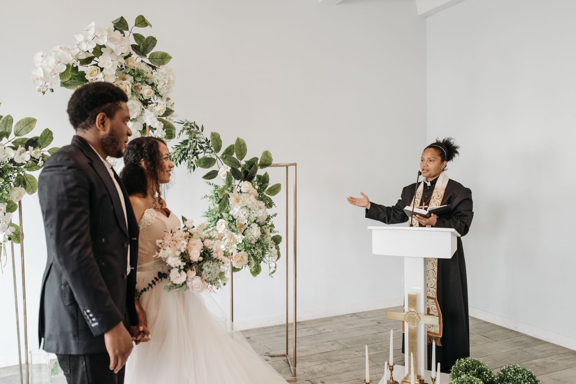 officiant speaking warmly to a couple during an outdoor ceremony, guests seated on either side, soft afternoon light