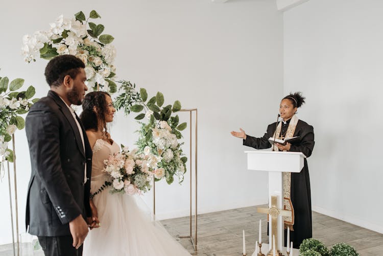 Female Pastor Speaking To Bride And Groom 