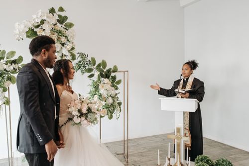Free A beautiful indoor wedding ceremony with a bride, groom, and pastor officiating in a floral setting. Stock Photo