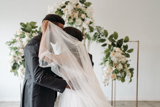 Newlywed couple sharing a romantic kiss under the veil with floral arrangements.