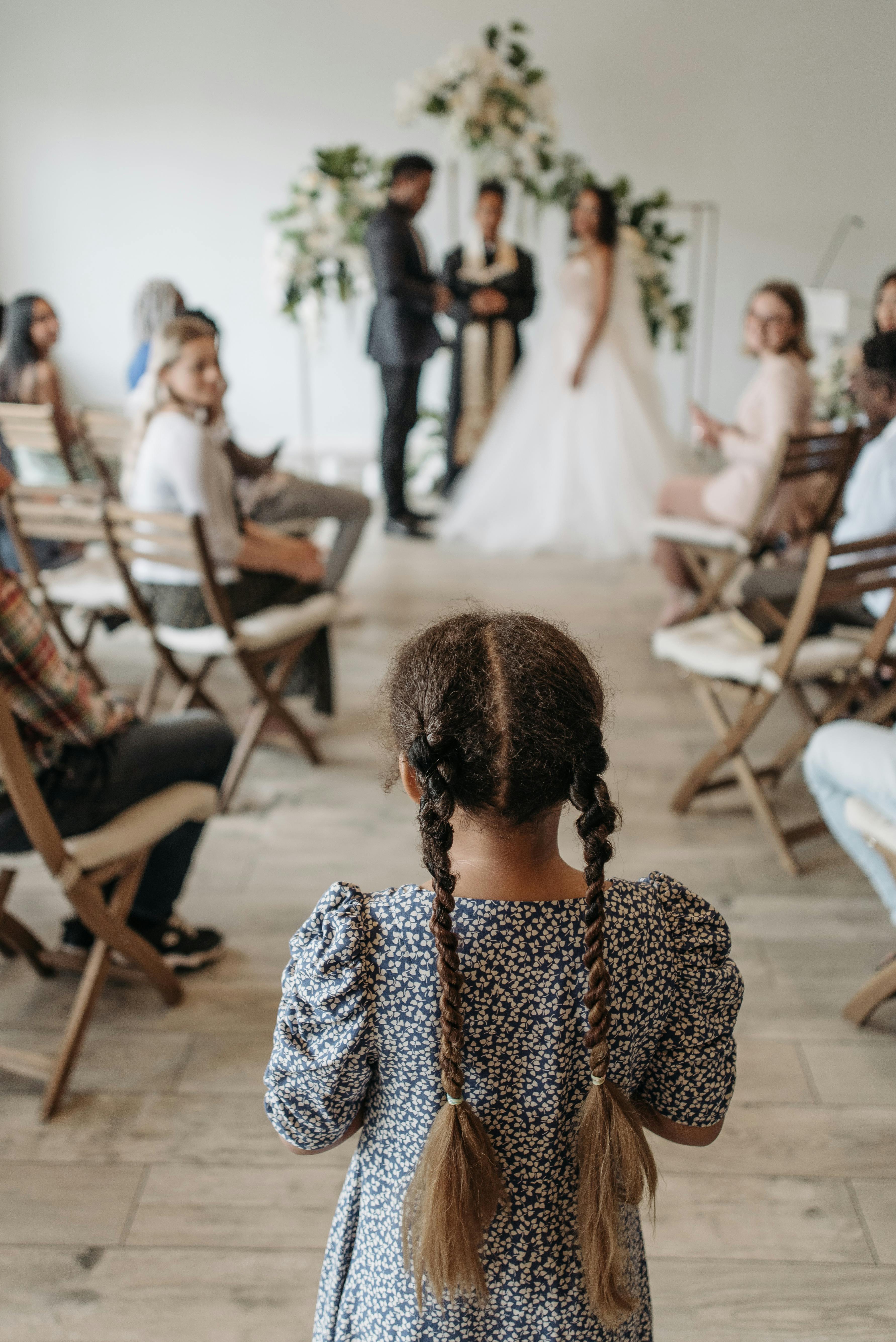 Bride and groom during indoor ceremony viewed from behind a young girl.