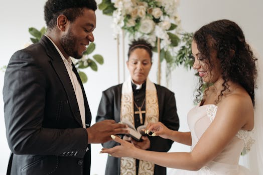 Bride and groom exchanging wedding rings indoors with pastor officiating.