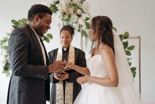 Free A diverse couple exchanging rings in an indoor wedding ceremony with a pastor officiating. Stock Photo
