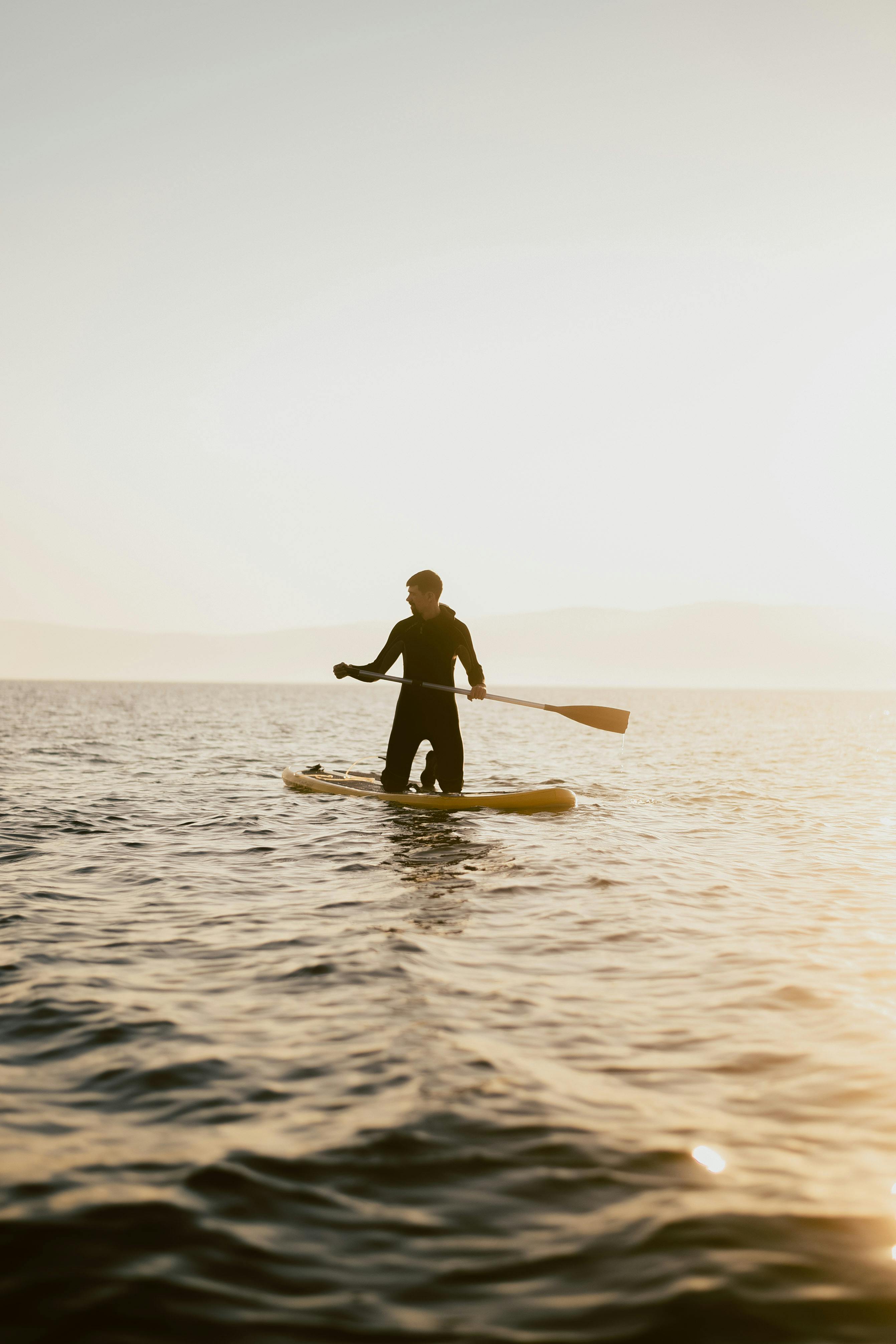 A silhouette of a man paddleboarding on calm waters during a beautiful sunset.