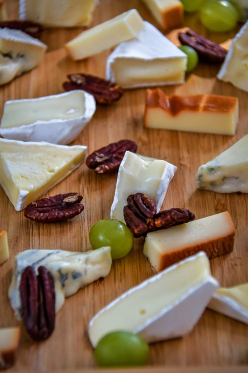 Free An assortment of gourmet cheeses and pecans on a wooden serving board. Stock Photo