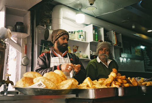 Two men selling fried snacks at an indoor street food stall, showcasing diverse food variety.